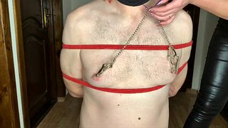 Mistress Nika tied up her slave and plays with his nipples with clamps, pouring hot wax on his tied penis
