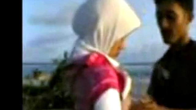 Ragazza indonesiana con hijab scopa sulla spiaggia